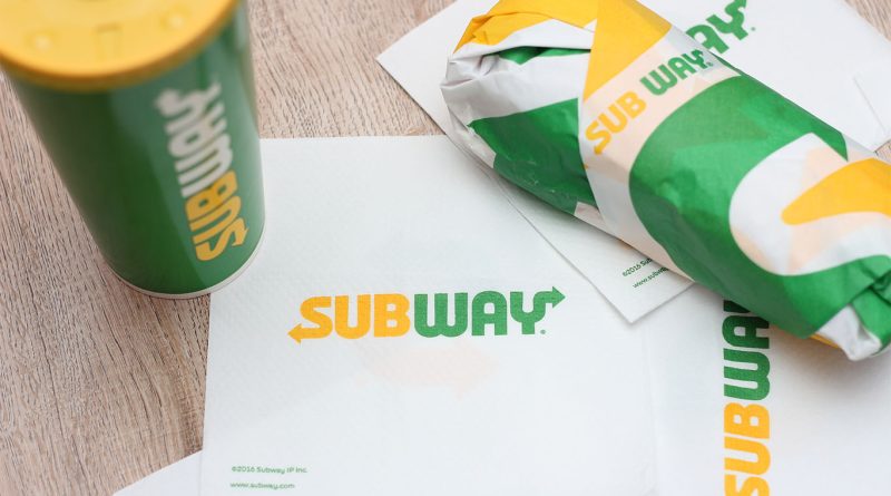 Subway sandwich, drink, and branded napkins on a wooden table.