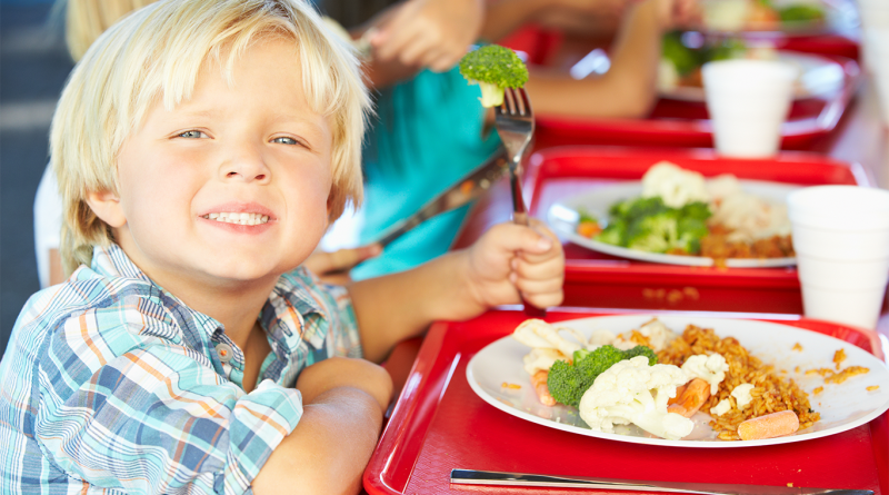 Image of a young school boy sat in a cafeteria with other children having their school lunch to support artificial food dyes ban article