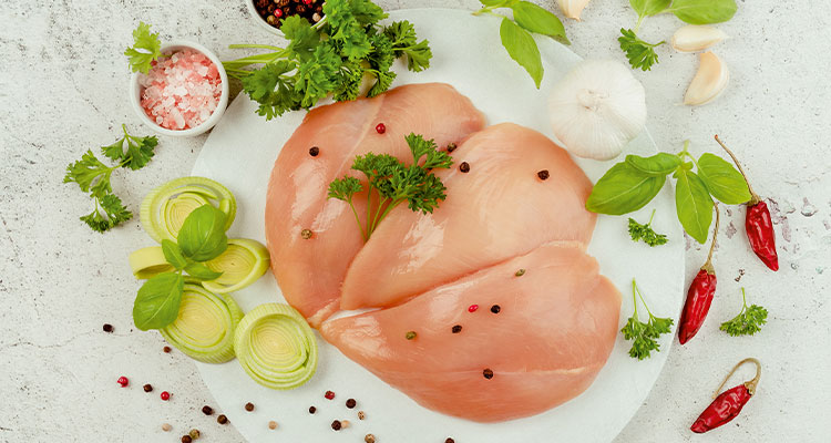 The central focus of the image is several pieces of raw, skinless, boneless chicken breast fillets arranged on a white plate