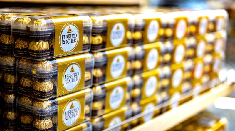 Alt Text: Stacks of Ferrero Rocher chocolate boxes neatly displayed on a store shelf, featuring the brand's signature gold and brown packaging.