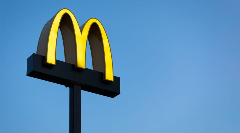 McDonald's golden arches logo illuminated against a clear blue sky, mounted on a tall black signpost