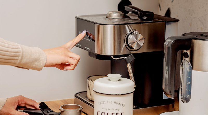 A person using a modern espresso machine on a kitchen counter, with a coffee canister, portafilter, and electric kettle nearby to support best coffee makers 2025 article
