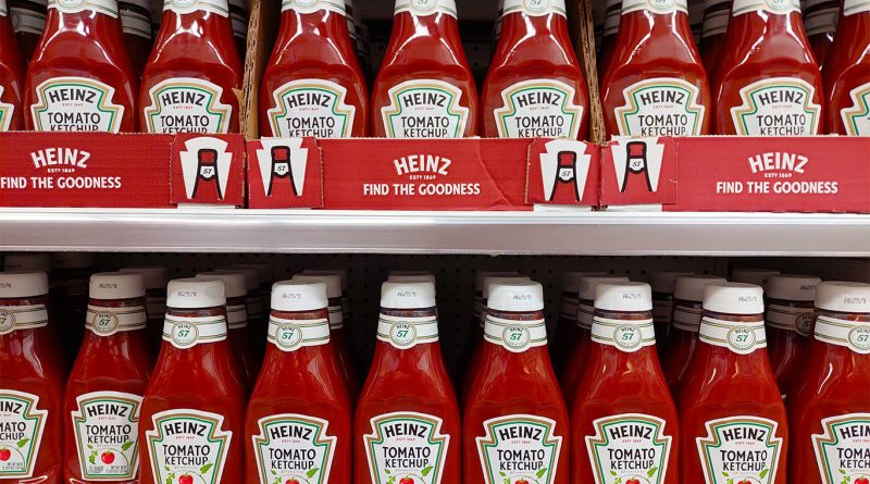 Rows of red Heinz Tomato Ketchup bottles are displayed on a shelf in a supermarket.