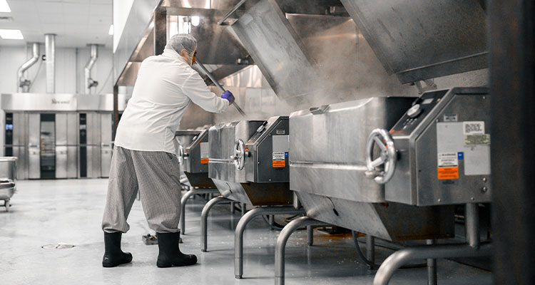 a person, dressed in a white jacket and uniform pants, working in a large, industrial food production facility
