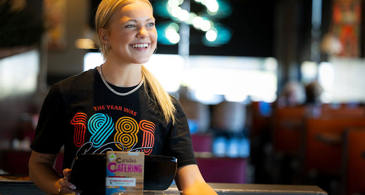 a person with blonde hair, pulled back into a ponytail, standing behind a counter