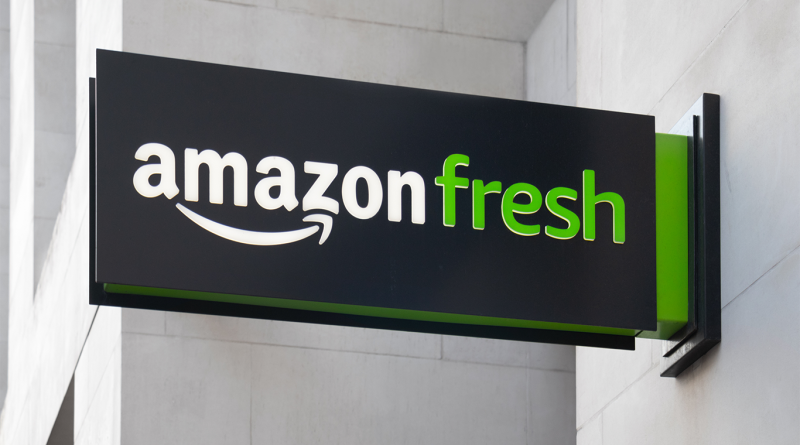 Amazon Fresh storefront sign mounted on a modern building exterior, featuring the brand's logo in white and green against a black background
