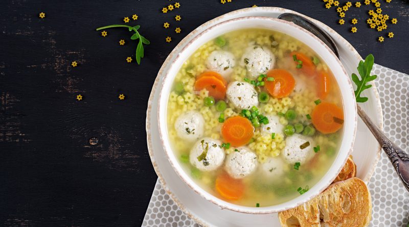 Bowl of Italian pastina soup with star-shaped pasta, carrots, peas, and chicken meatballs served with toasted bread
