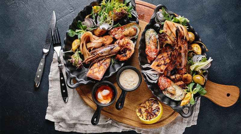 Grilled seafood platter with shrimp, salmon, mussels and squid served with fresh greens, sauces and grilled lemon on cast iron dishes.