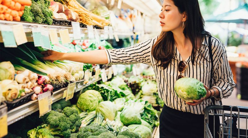 Person shopping for groceries while checking a list and comparing prices in-store