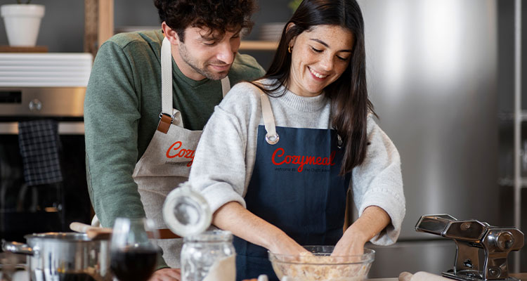two people wearing Cozymeal branded aprons while preparing food in a kitchen