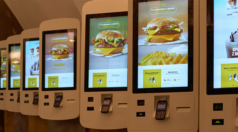 Self-service McDonald’s ordering kiosks displaying burger and dessert menu items inside a modern restaurant interior.